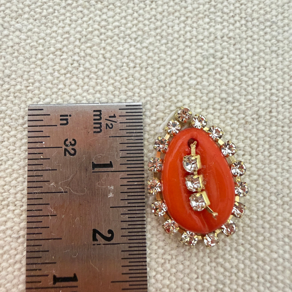 Decorative brooch with coral-like center and gold accents next to a ruler for scale on a textured beige background