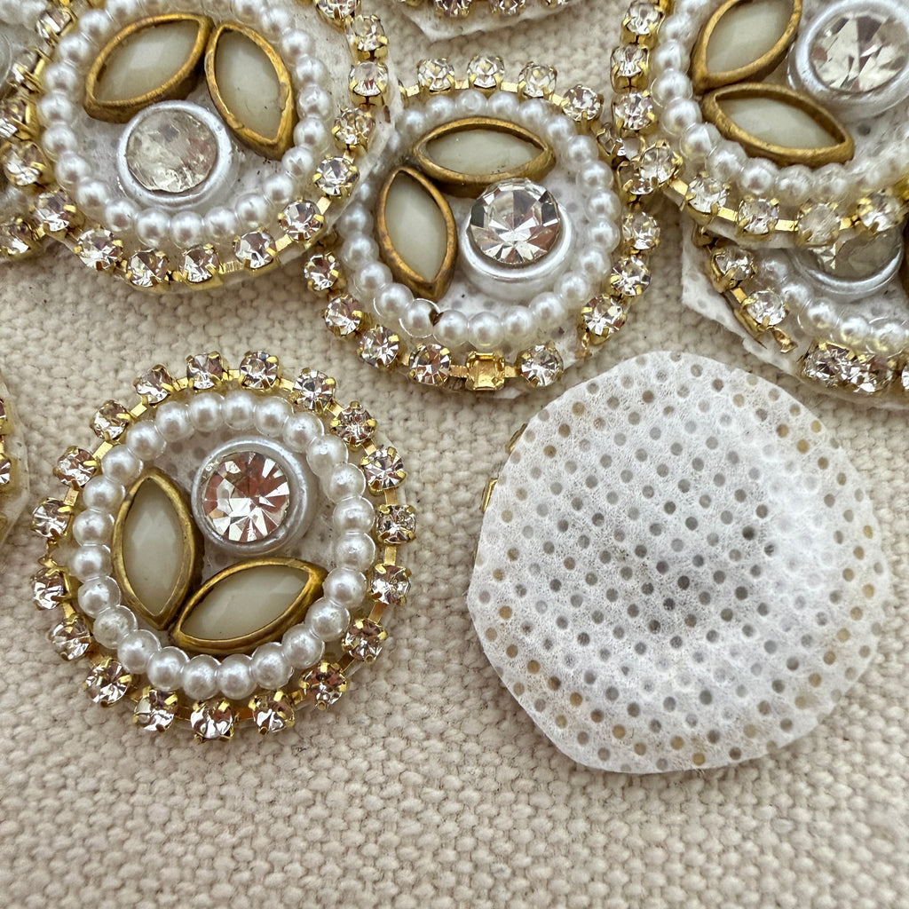 Close-up of decorative buttons with pearls and crystals on a textured beige surface