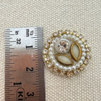 Decorative brooch with pearls and crystals next to a ruler on a textured beige background