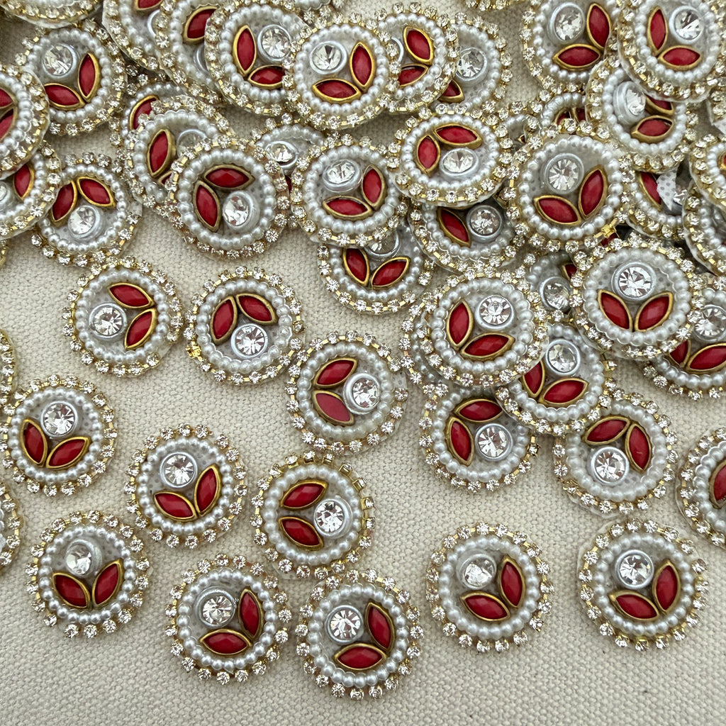 Close-up of decorative buttons with red centers, pearls, and crystals on a beige background