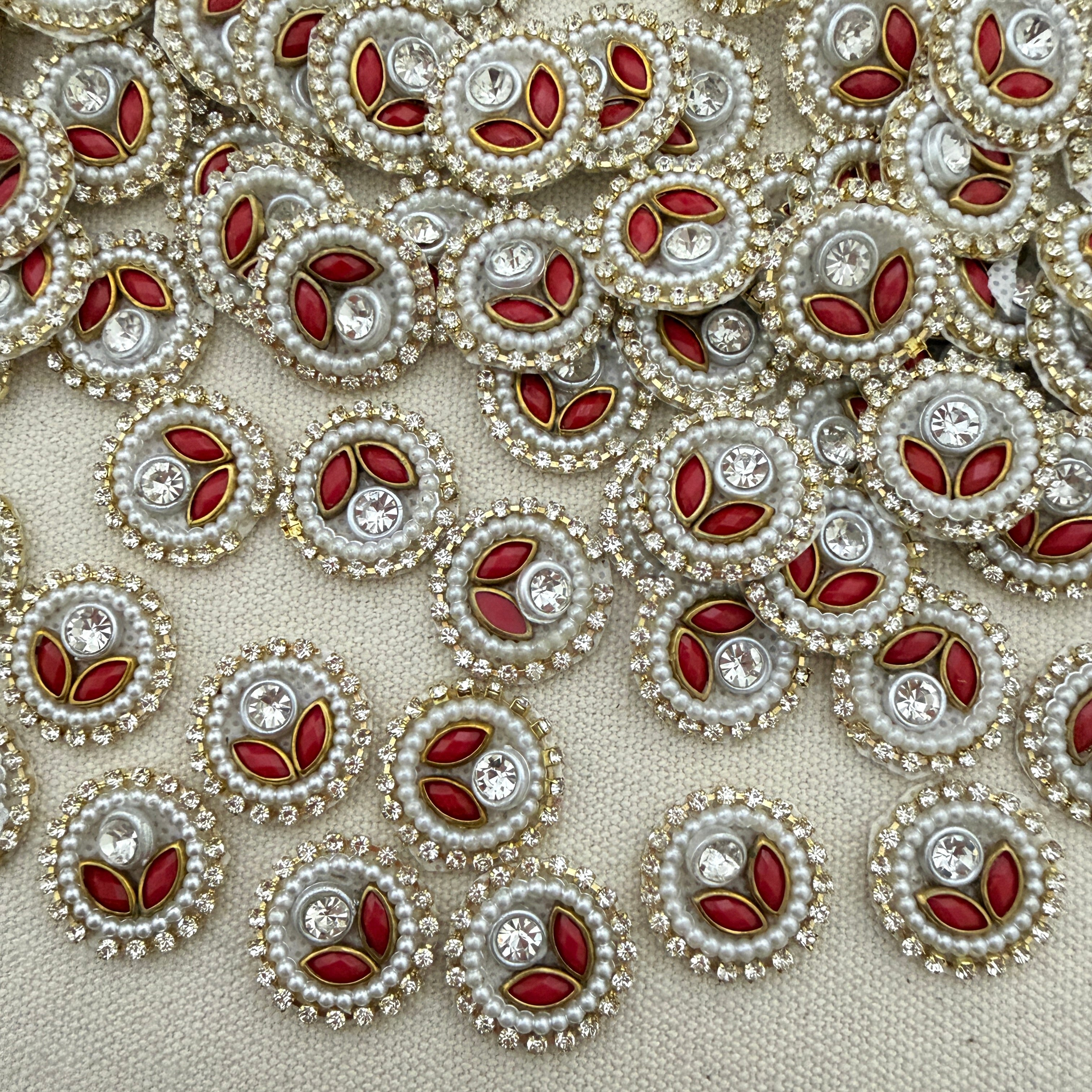 Close-up of decorative buttons with red centers, pearls, and crystals on a beige background