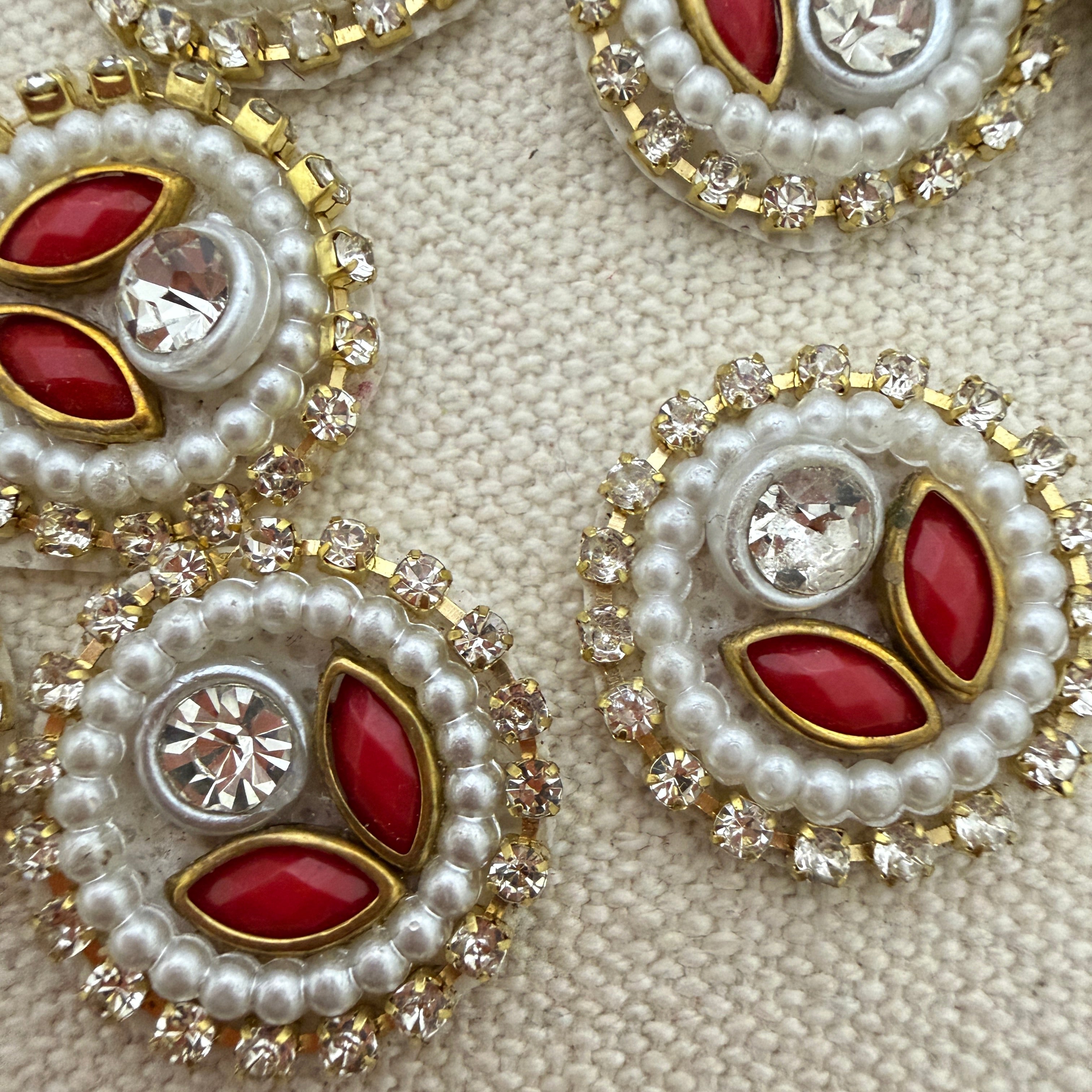 Close-up of decorative brooches with red stones, pearls, and crystals on a textured beige background.