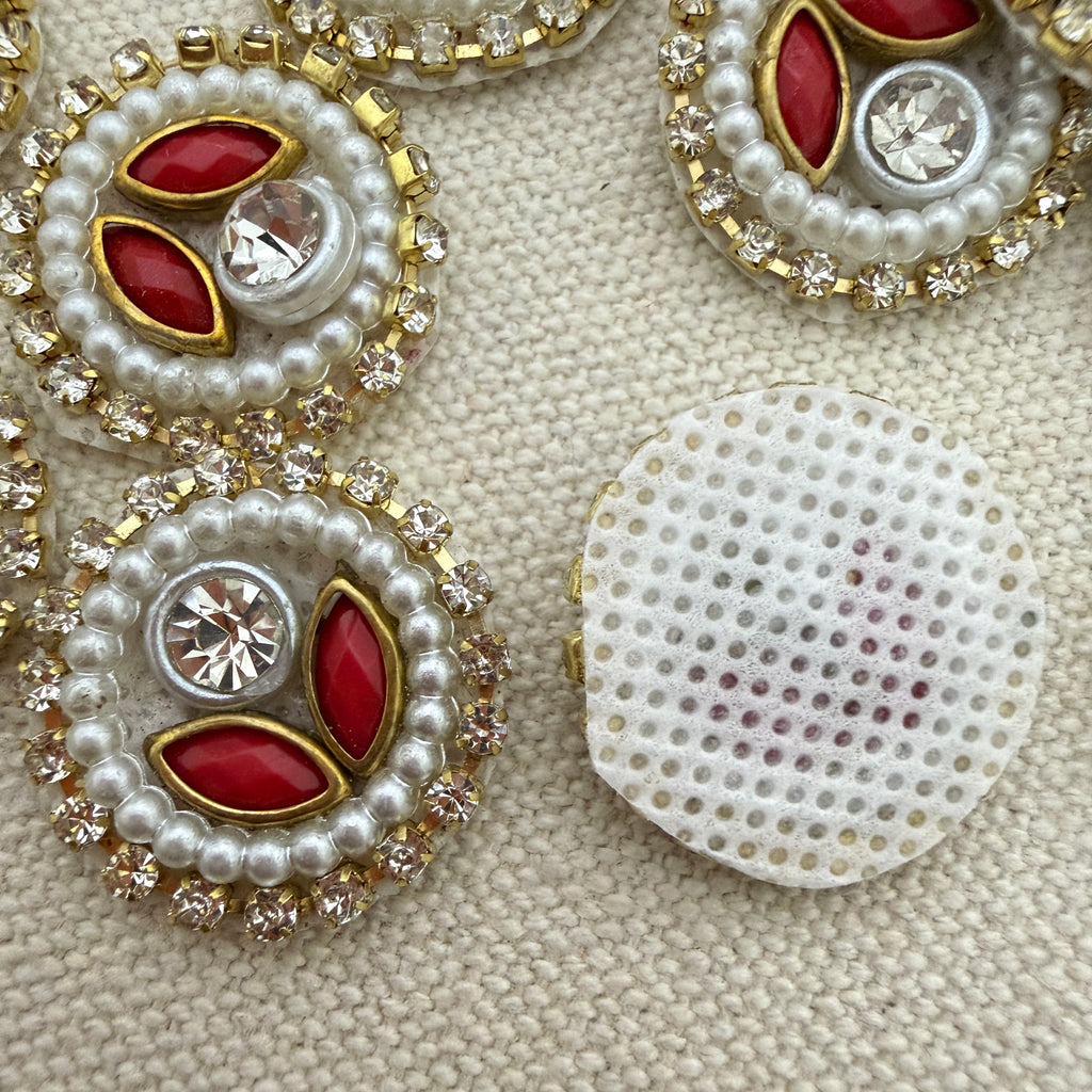 Decorative buttons with red stones, pearls, and crystals on a beige fabric background