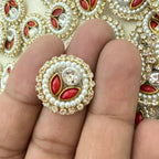 Decorative ring with pearls and red stones on a finger, with a patterned background.
