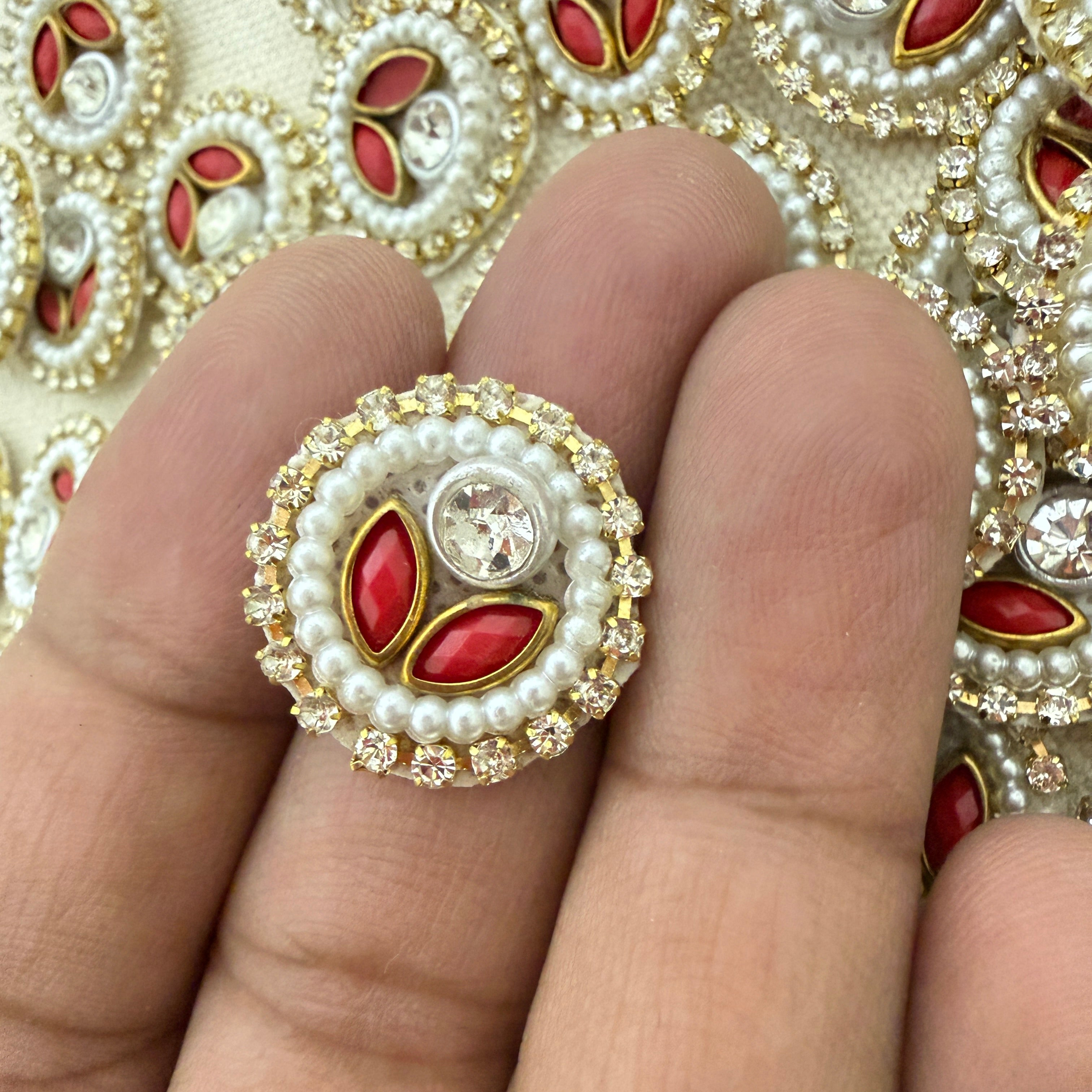 Decorative ring with pearls and red stones on a finger, with a patterned background.