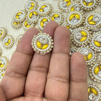 Decorative gemstone with yellow and white elements held between fingers against a patterned background