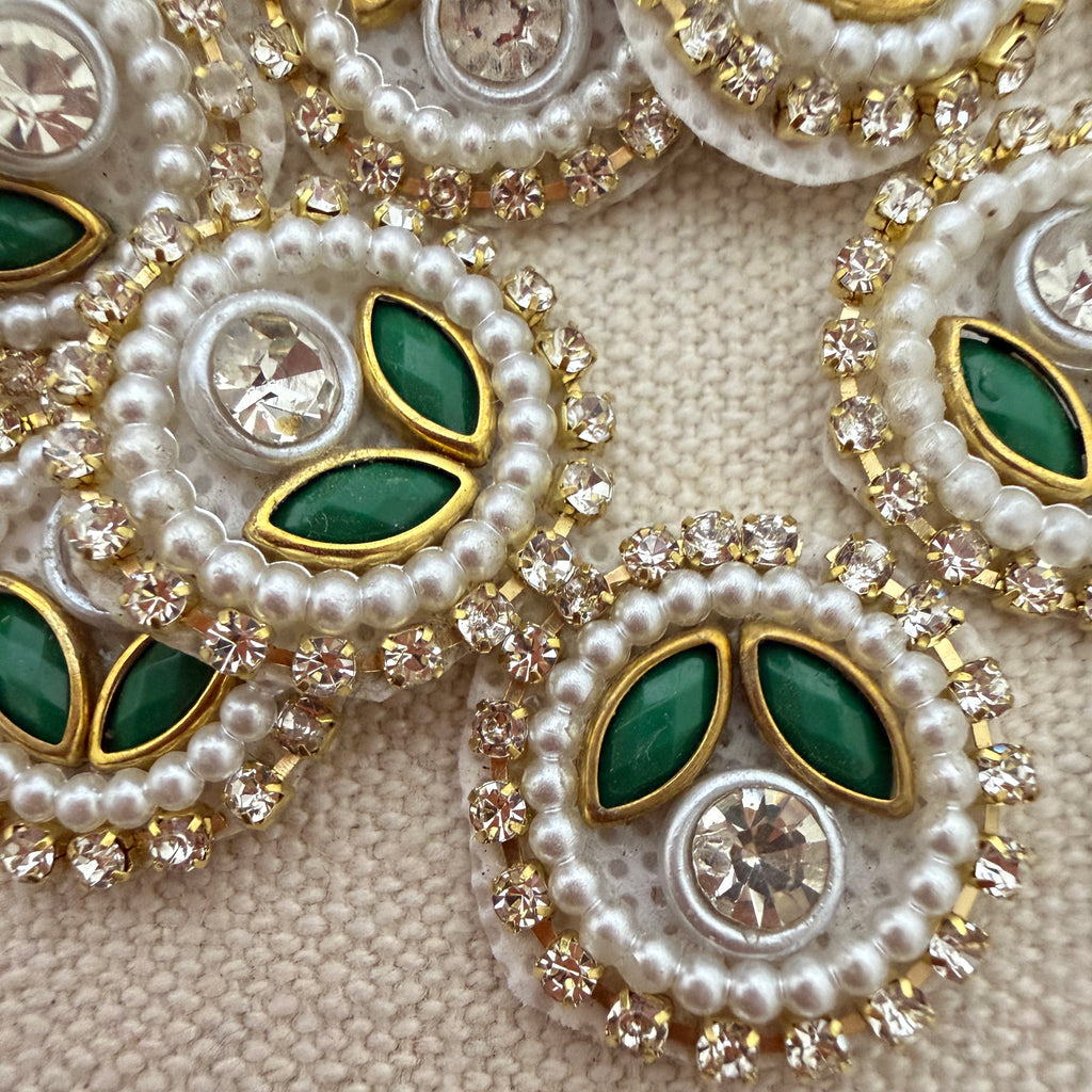 Close-up of decorative jewelry with pearls, green stones, and crystals on a beige background