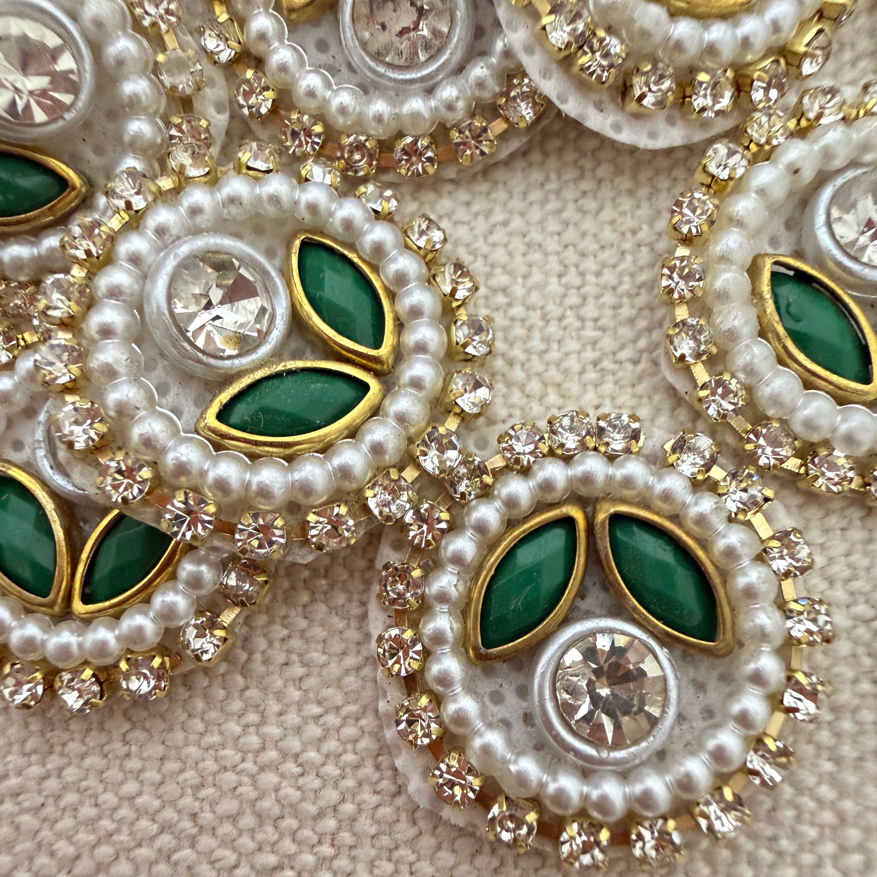 Close-up of decorative jewelry with pearls, green stones, and crystals on a beige background