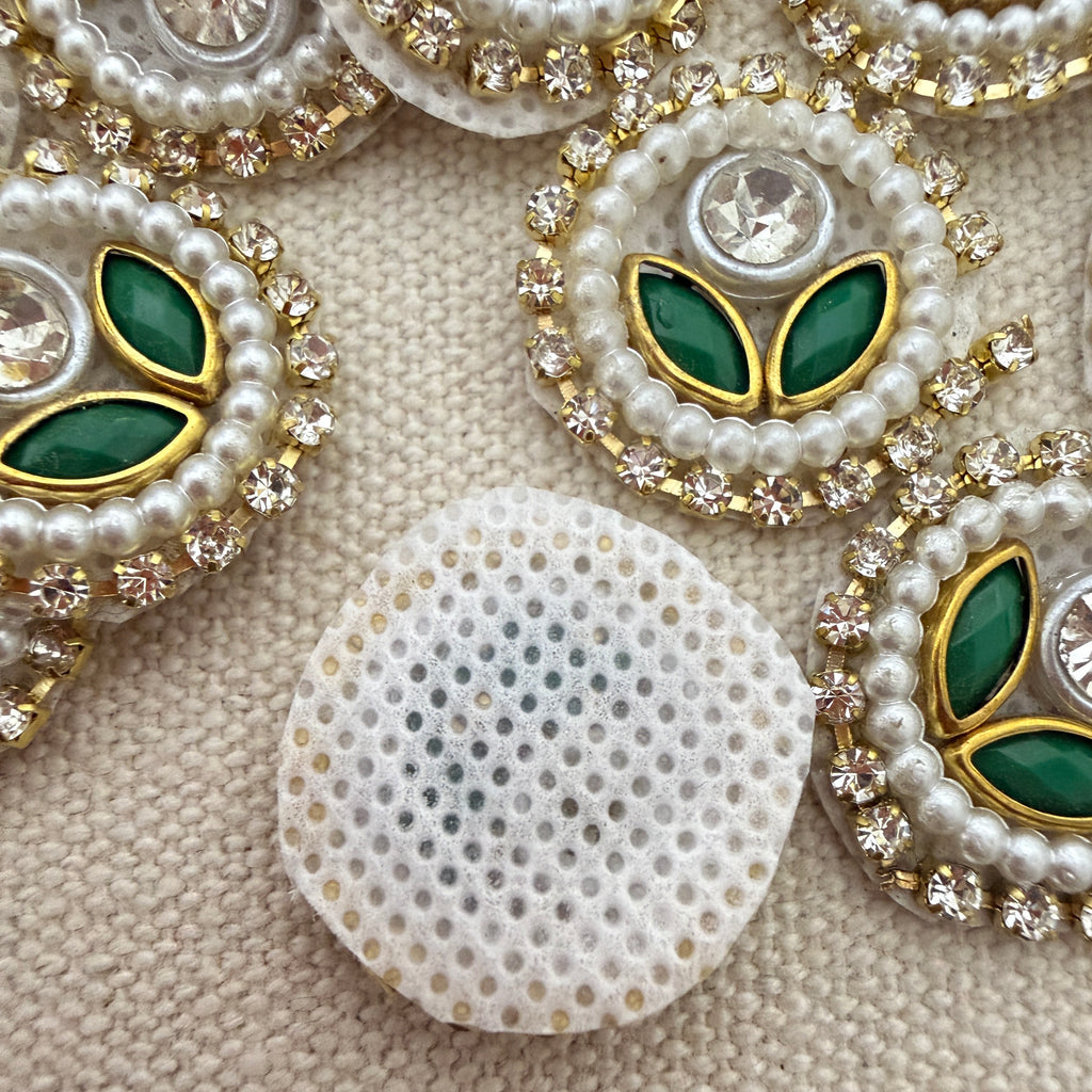 Decorative buttons with pearls, green stones, and gold accents on a textured beige background.