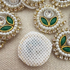 Decorative buttons with pearls, green stones, and gold accents on a textured beige background.