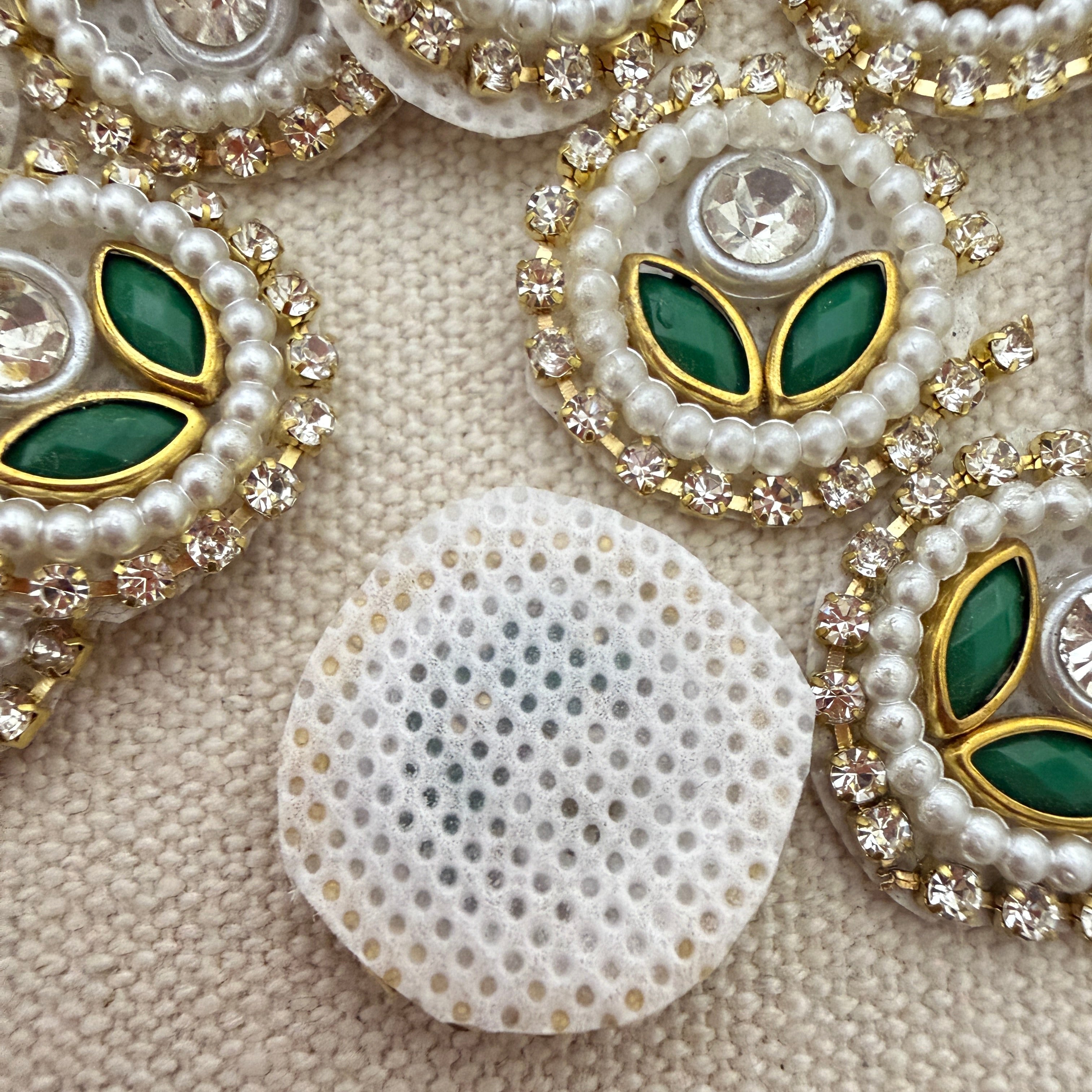 Decorative buttons with pearls, green stones, and gold accents on a textured beige background.