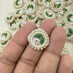 Decorative brooch with pearls and green stones held between fingers against a patterned background