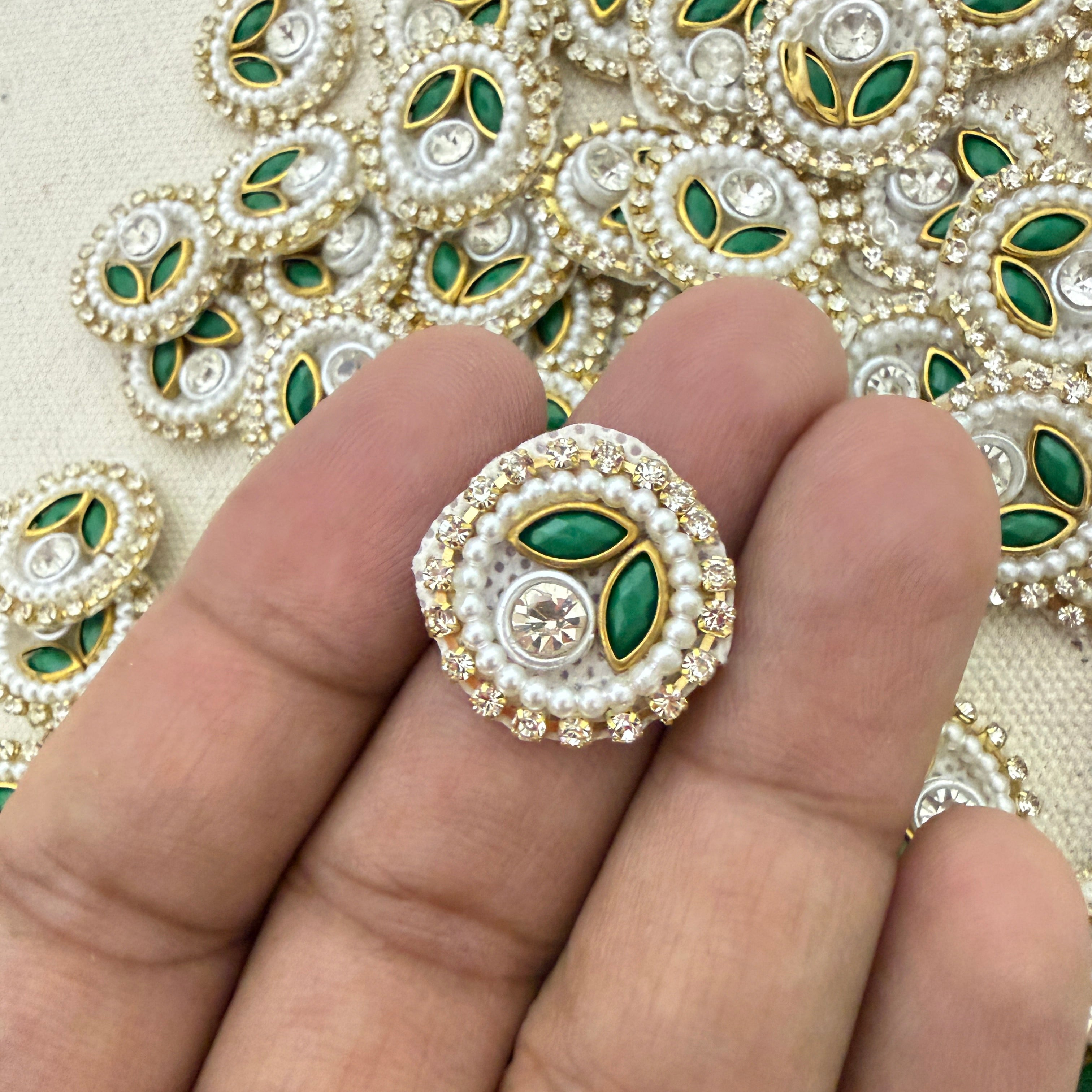 Decorative brooch with pearls and green stones held between fingers against a patterned background