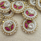 Close-up of decorative buttons with pearls, crystals, and pink stones on a beige fabric background.