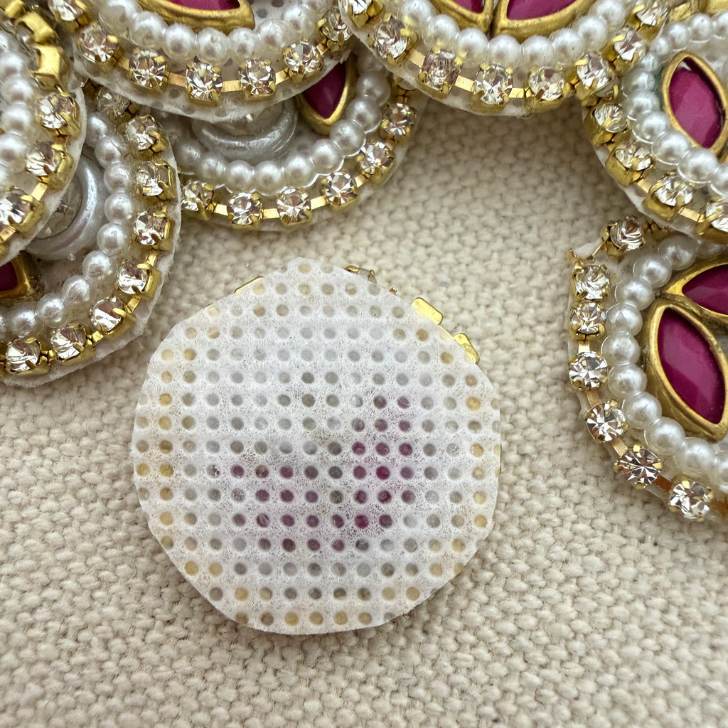 Close-up of decorative buttons with pearls and gemstones on a textured beige background