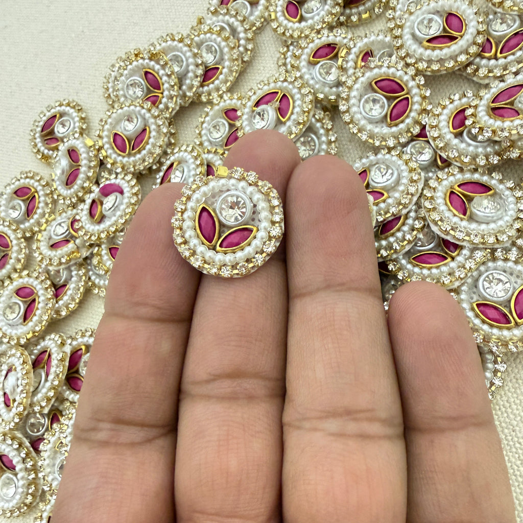 Decorative button with pink and gold details held between fingers against a patterned background