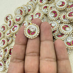 Decorative button with pink and gold details held between fingers against a patterned background