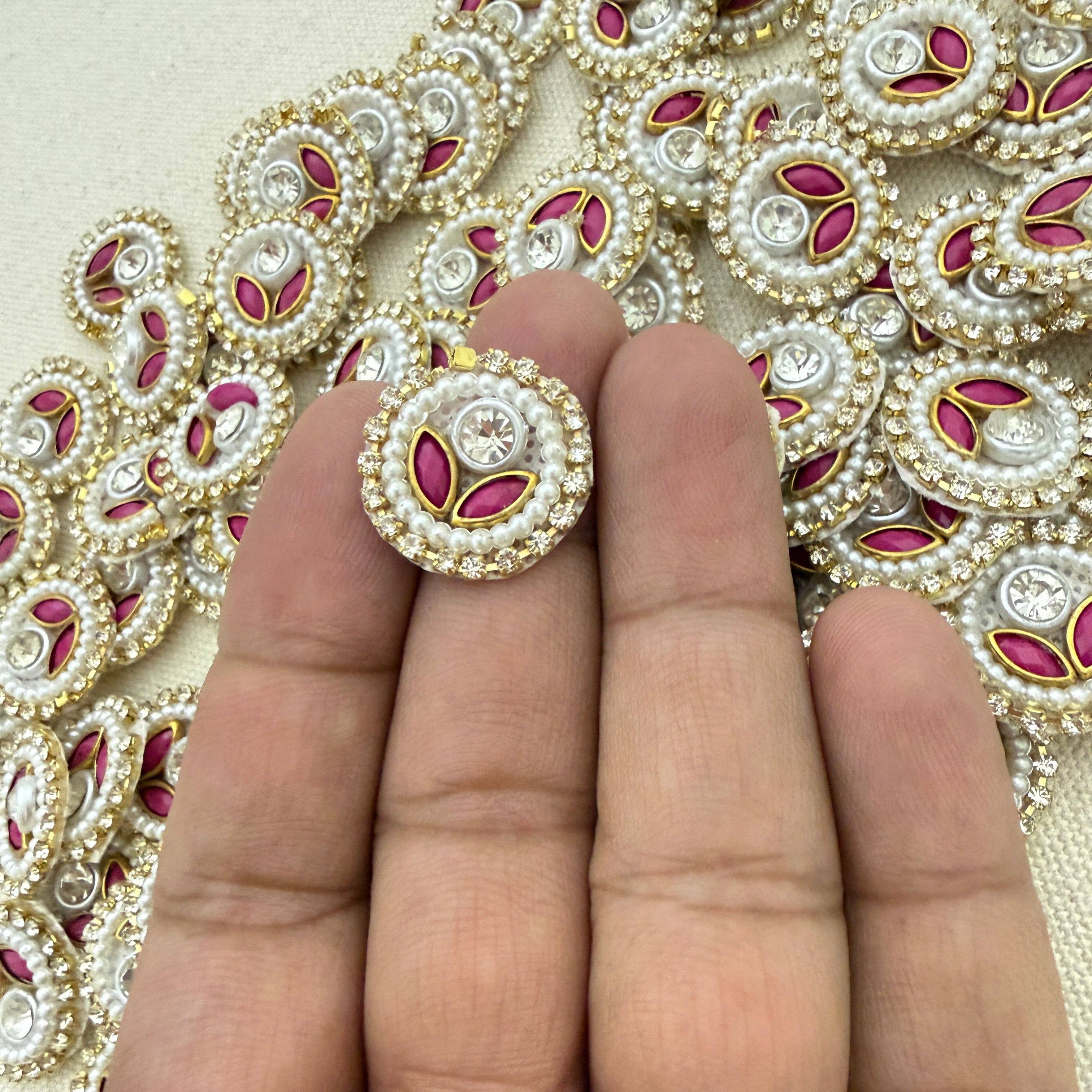 Decorative button with pink and gold details held between fingers against a patterned background