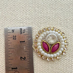 Decorative button with pink leaves and pearl details next to a ruler for scale on a textured beige background