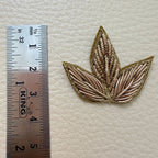 Reverse side of a gold three-leaf floral fabric patch showing the backing