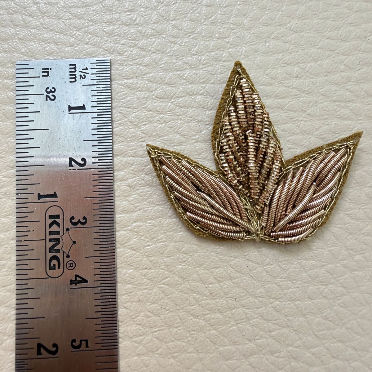 Reverse side of a gold three-leaf floral fabric patch showing the backing