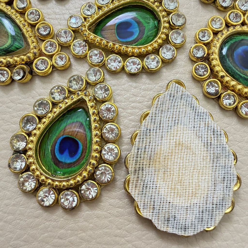 Close-up of two green and blue peacock-eye teardrop patches with clear rhinestone borders