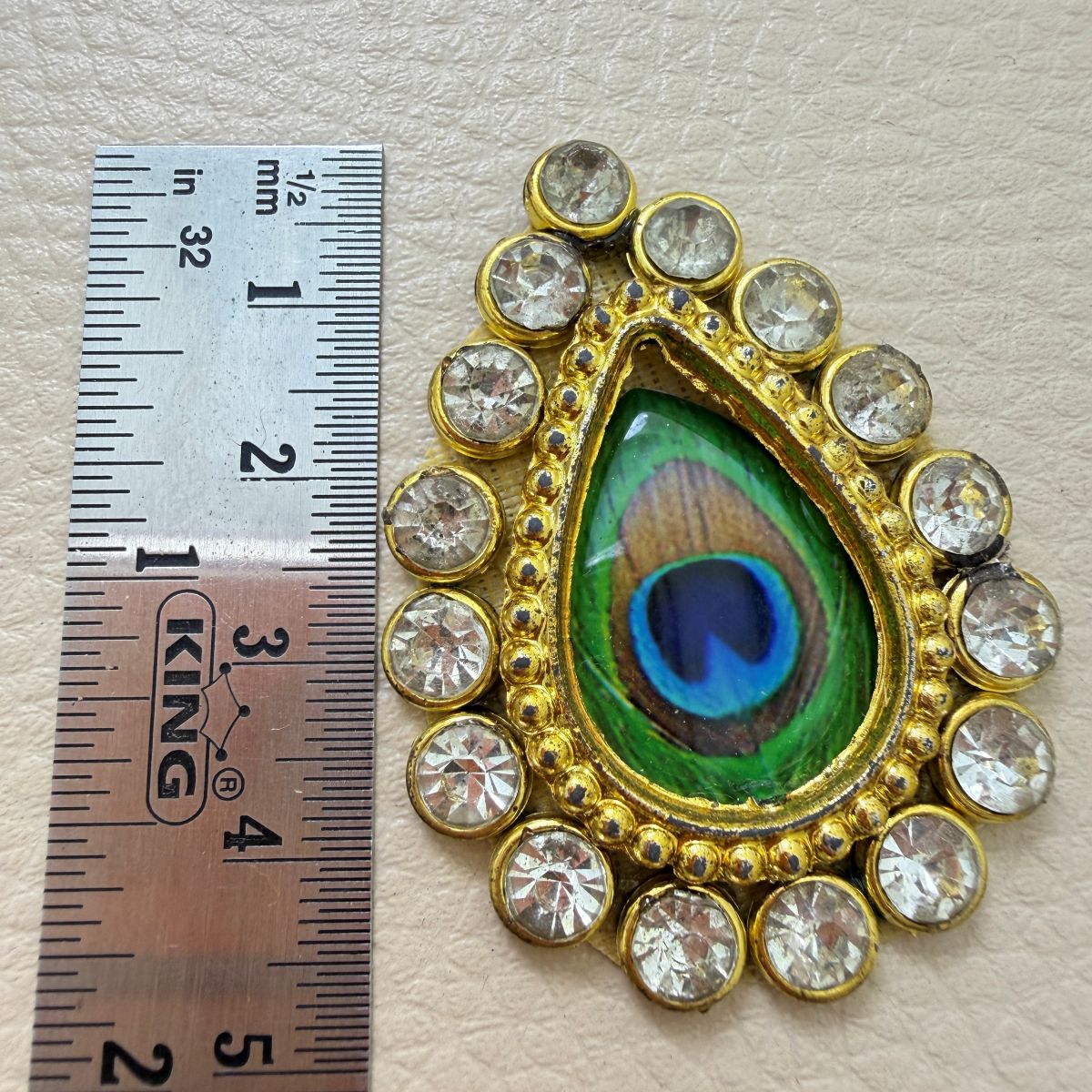 Teardrop peacock-eye rhinestone patch held in hand to show scale