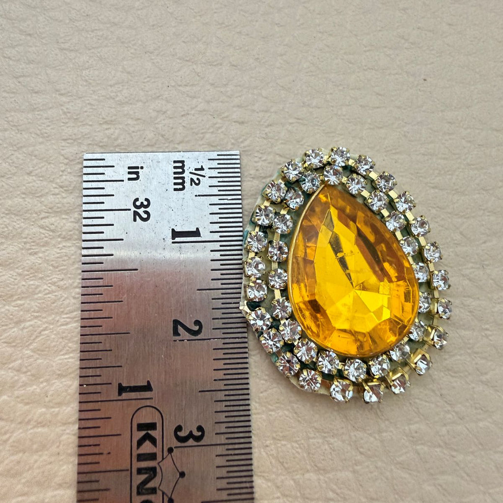 Amber gold teardrop patch beside a ruler showing approximate size