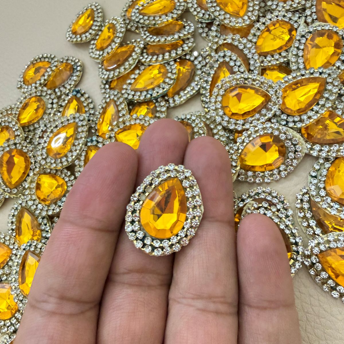 Hand holding an amber gold teardrop rhinestone patch for scale