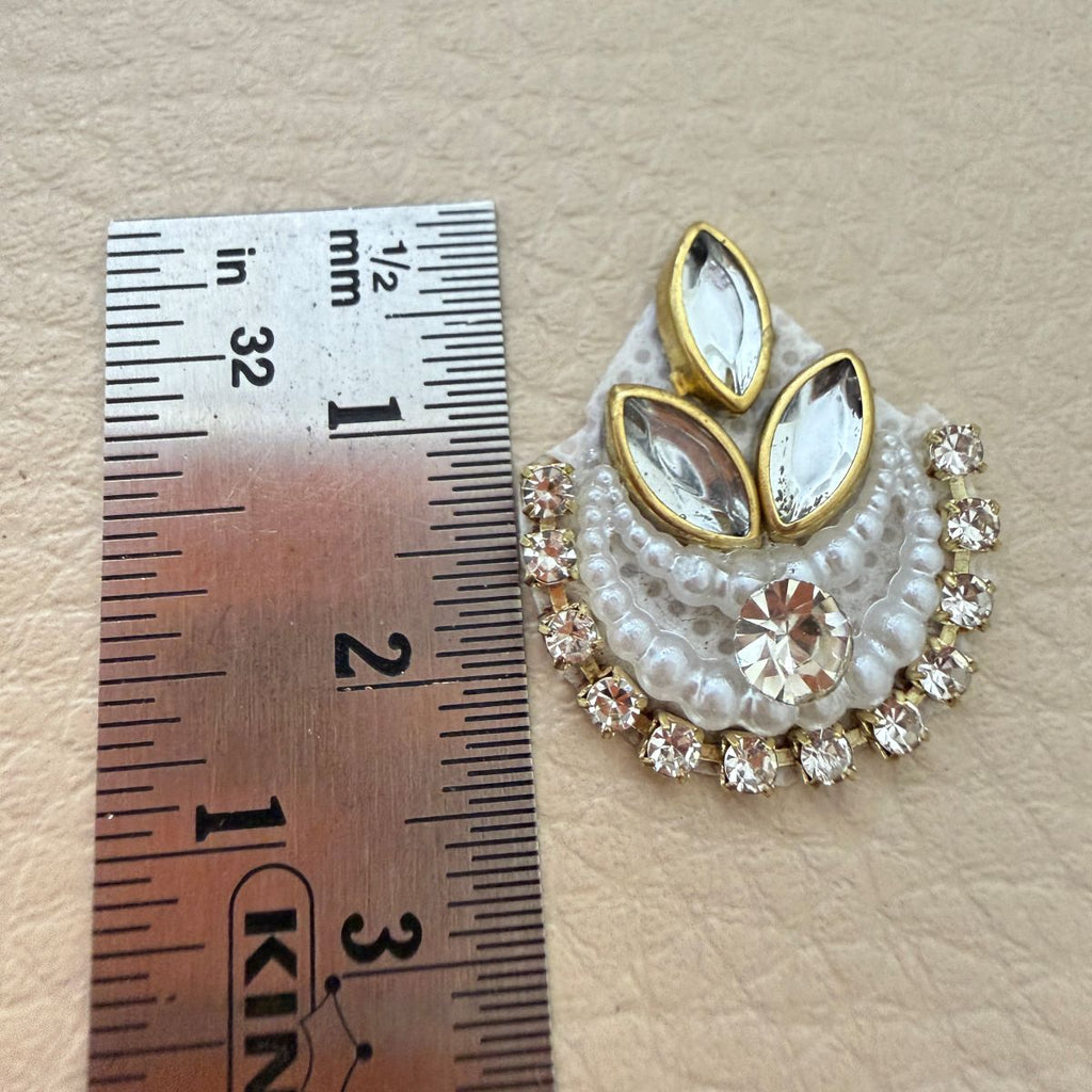 Close view of two white beaded crescent patches with crystal centers and gold-tone accents