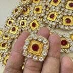 Hand holding ornate square gold-tone patch with ruby red center and clear crystal halo