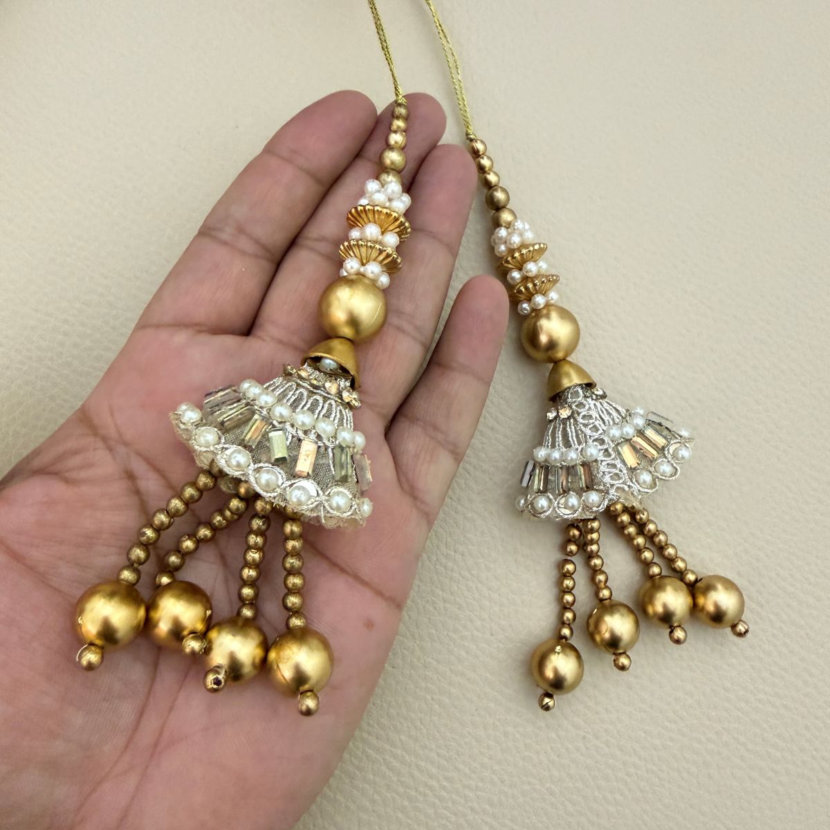 Two gold and silver pearl latkan tassels shown in hand for scale