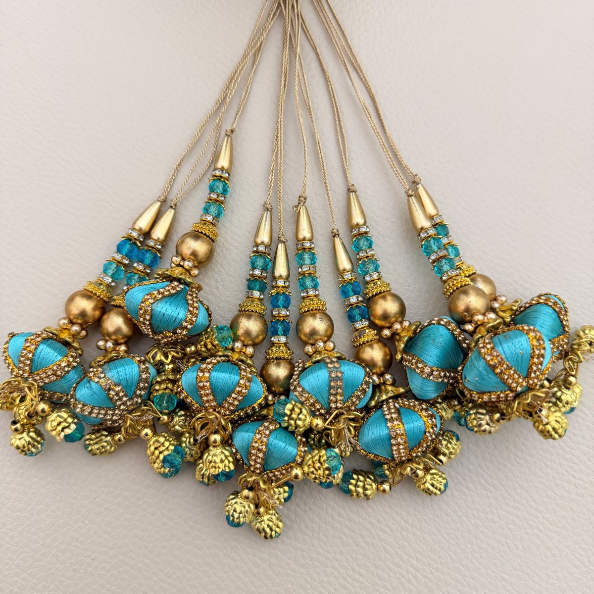 Hand holding turquoise and antique gold beaded latkan tassel to show scale
