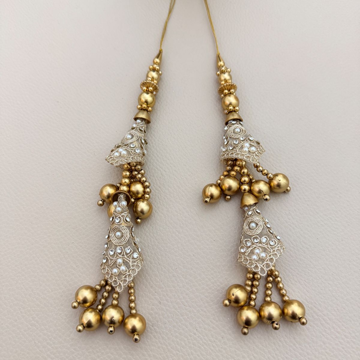 Two gold and silver embroidered tassel latkans beside a ruler