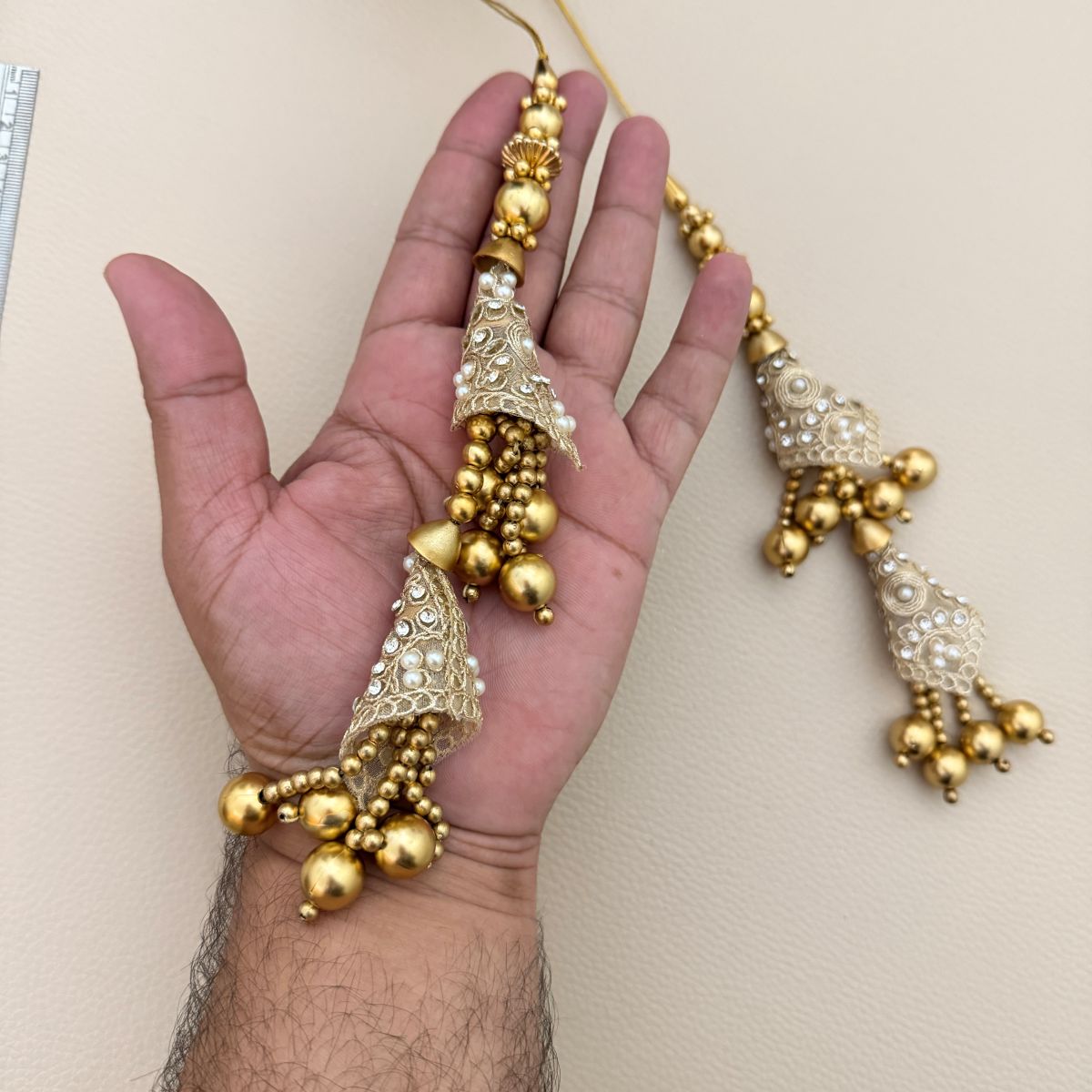 Hand holding an ornate gold and silver double tassel latkan