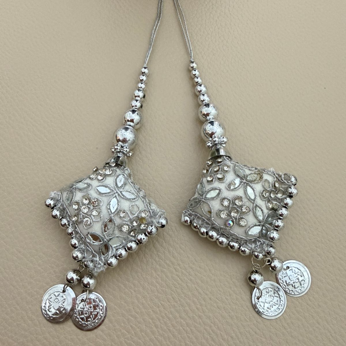 Pair of silver square latkan tassels with floral embroidery, beads and coin charms shown beside a ruler