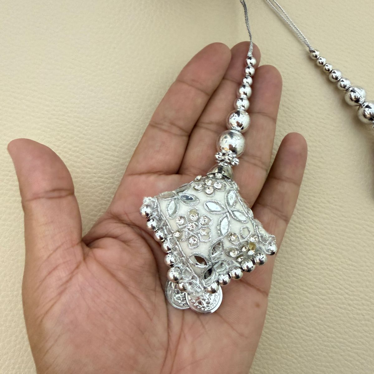 Close-up of one silver embroidered square latkan tassel with beaded cord shown in hand