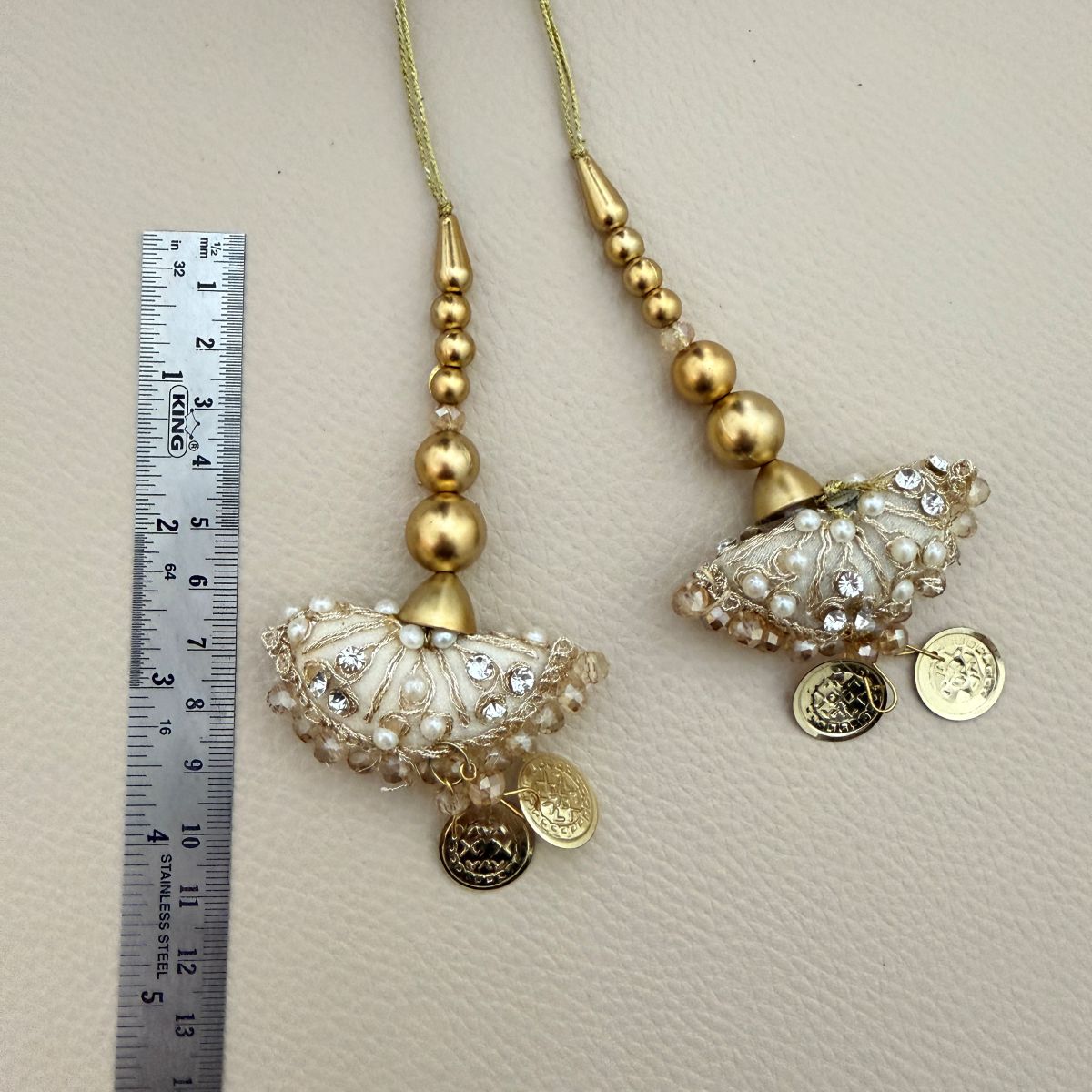 Close view of ivory fan-shaped tassels with gold embroidery, pearl beads, crystals and coin charms