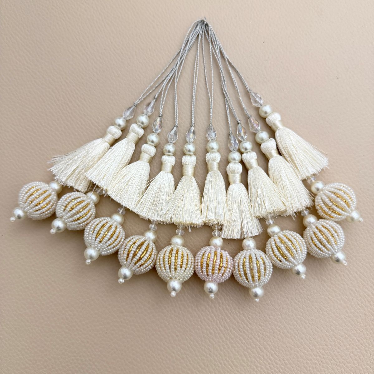 Close-up of ivory thread fringe, pearl-look beads, clear crystals and gold striped seed-bead ball