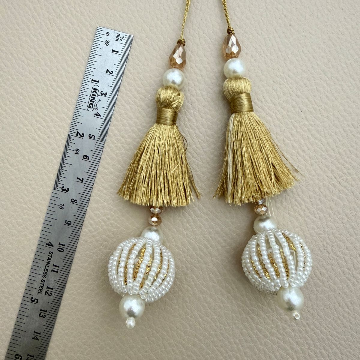 Two gold fringe tassels with white and gold striped beaded balls and pearl-look accents