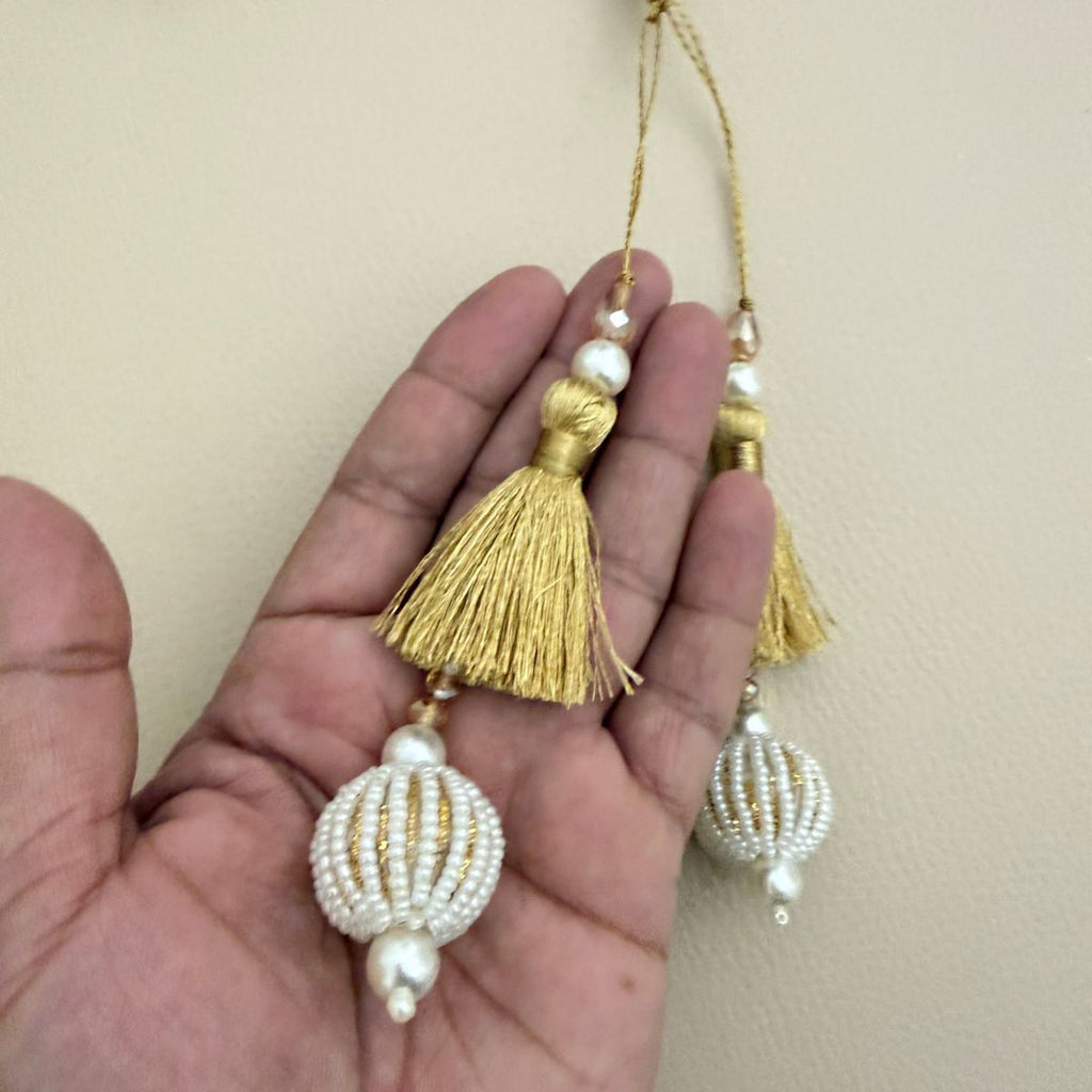 Gold thread and white beaded ball latkan tassels shown in hand for scale