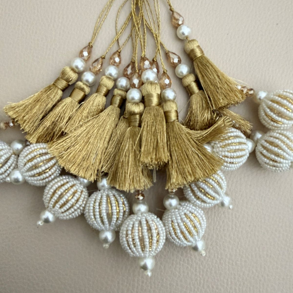 Gold thread and white seed-bead ball tassels beside a ruler showing approximate decorative drop