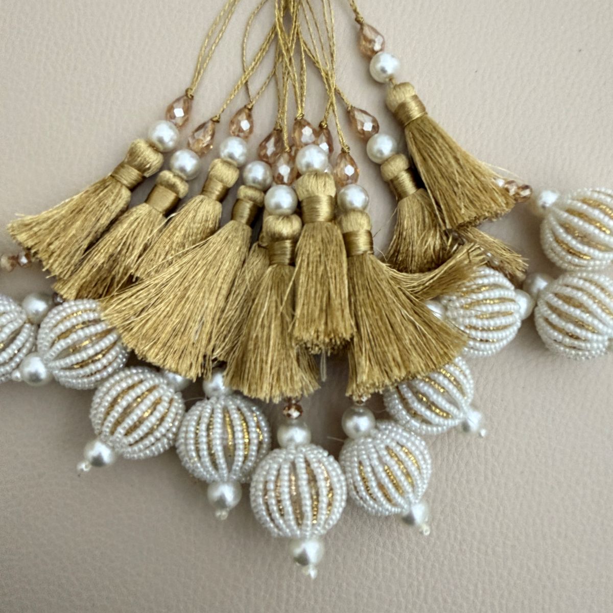 Gold thread and white seed-bead ball tassels beside a ruler showing approximate decorative drop