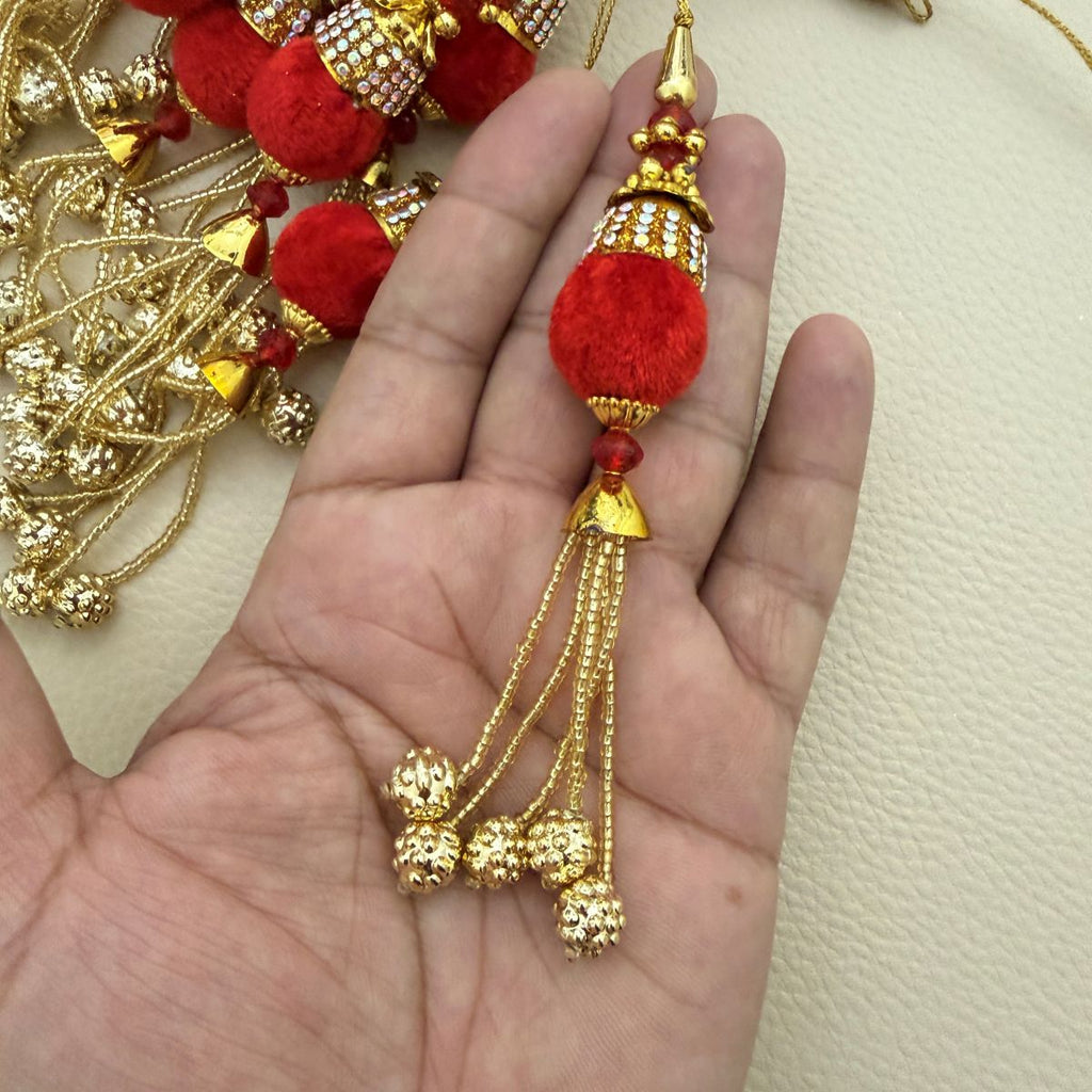 Close view of red textured textile ball, embellished cap, red beads and gold-tone tassel chains
