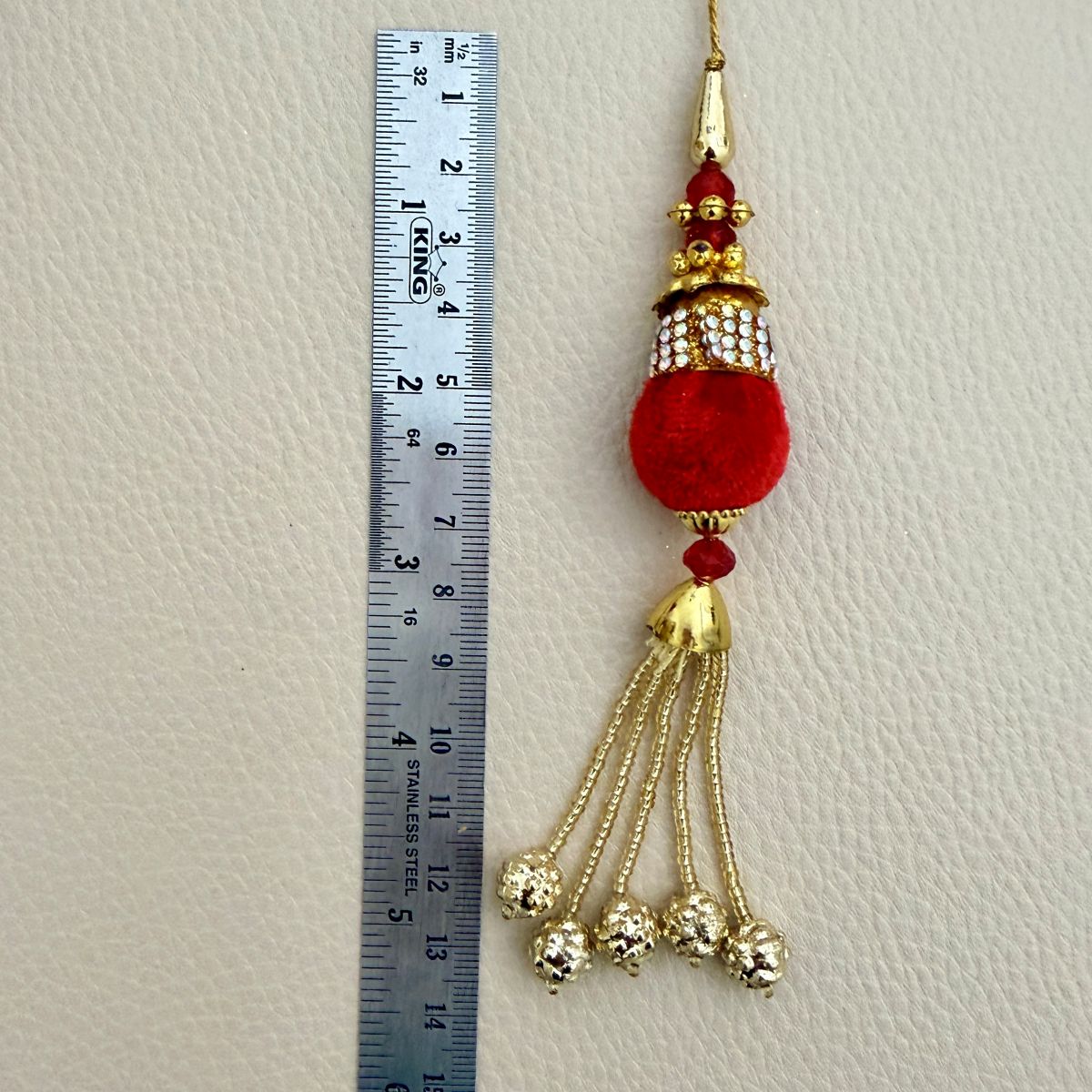 Red and gold beaded chain latkan tassel beside a ruler showing approximately 13 centimeters