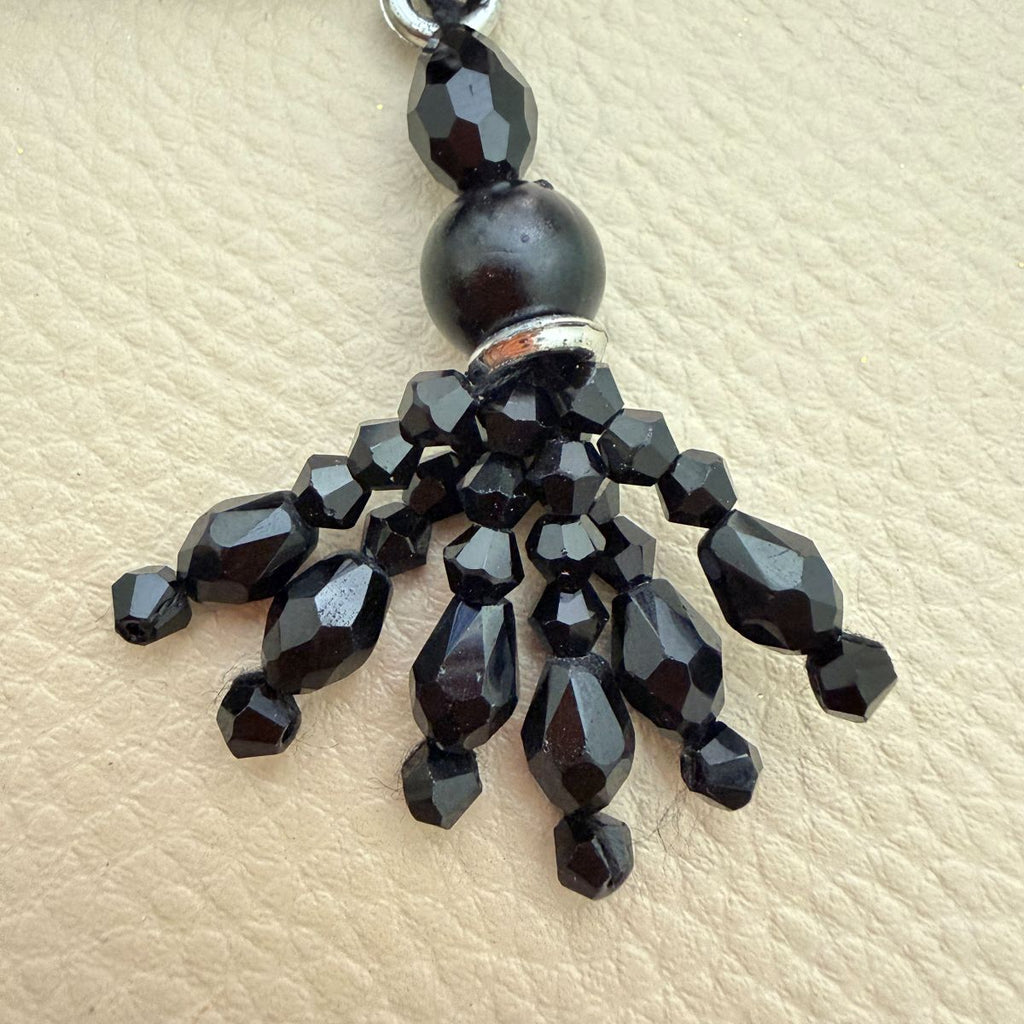 Black beaded tassel charm shown beside a ruler
