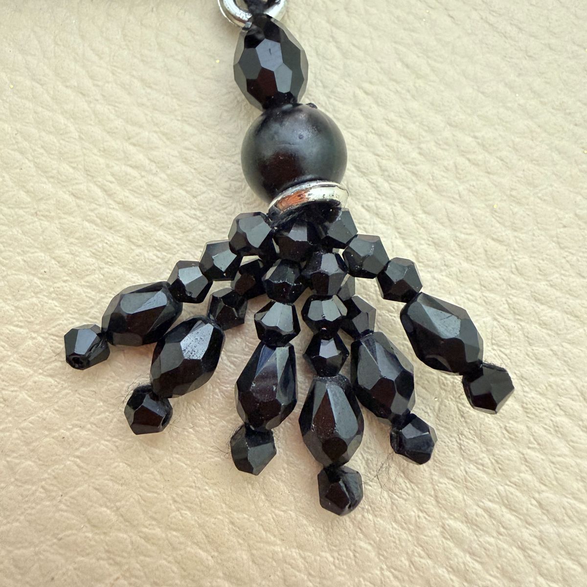 Black beaded tassel charm shown beside a ruler