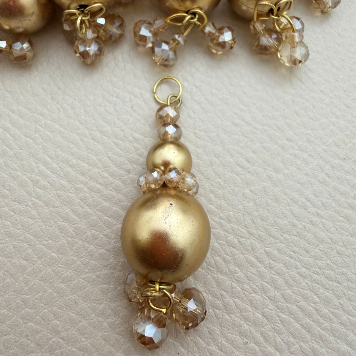 Gold pearl-look and champagne faceted bead tassel shown in hand for scale