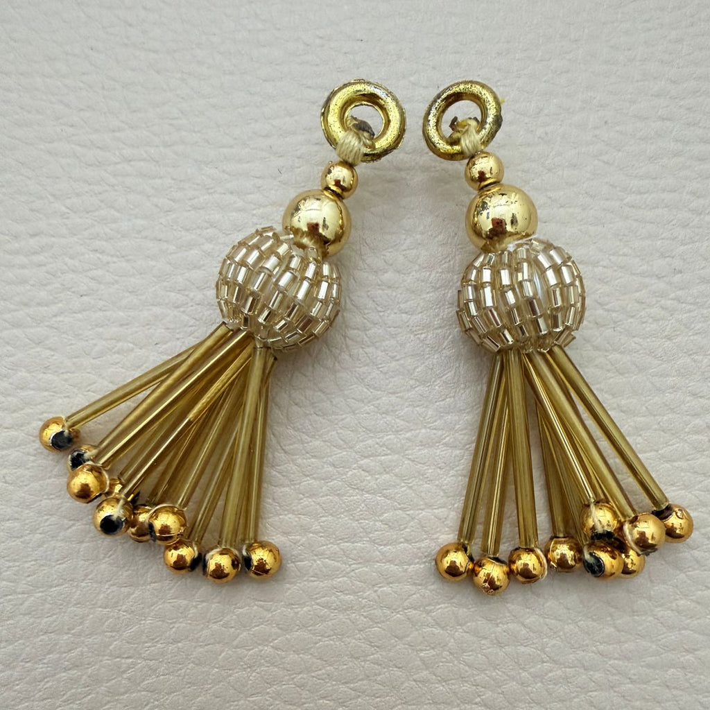 Gold metallic beaded tassel charm held in hand showing woven center and fan-shaped drops