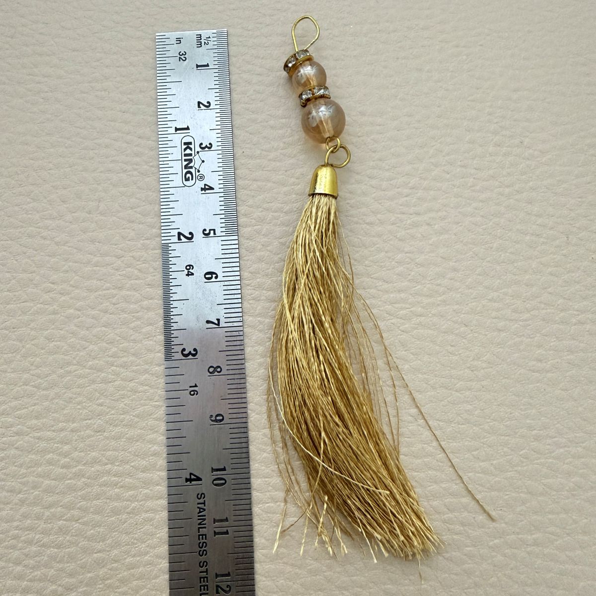 Gold thread tassel photographed beside a ruler for approximate size reference
